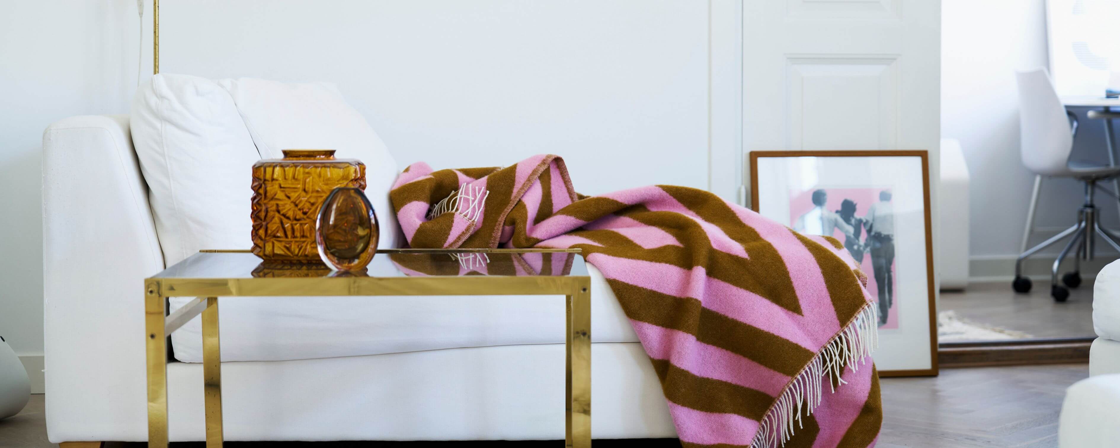 White sofa with a Klippan Tangent pink and caramel striped blanket, gold coffee table, and decorative items in a living room.